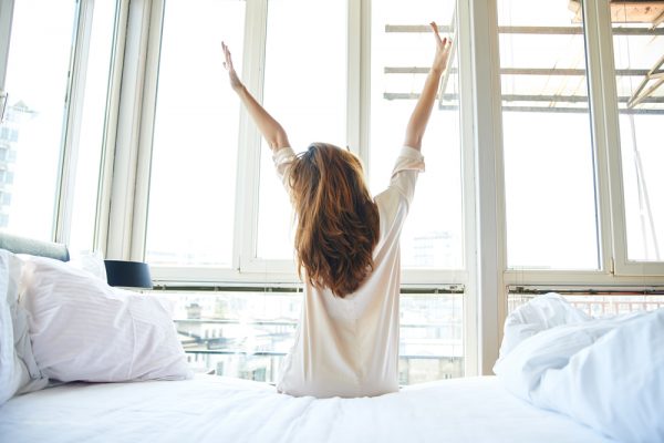 woman with long brown hair stretching after waking up in a bright room